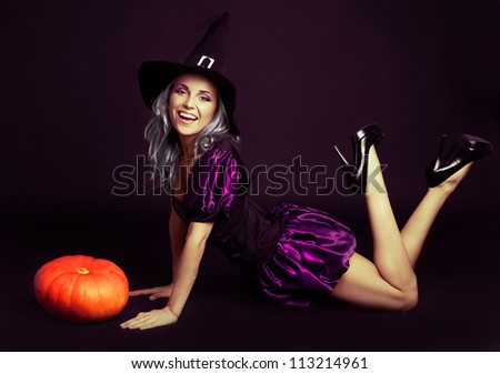 happy young witch with  a pumpkin, against dark studio background