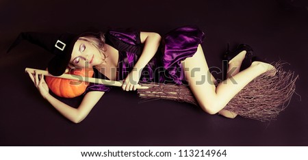 beautiful sleeping witch with a pumpkin and broom, against dark studio background