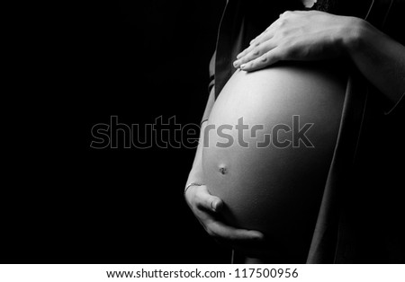 black and white picture of the belly of a pregnant woman, isolated on black studio background