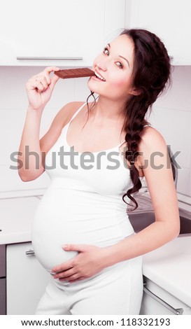 beautiful young pregnant woman eating chocolate at home in the kitchen