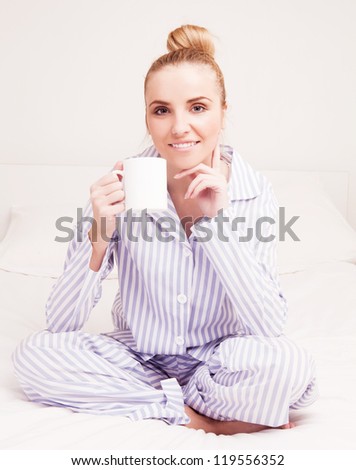 beautiful young woman wearing pajamas drinking coffee in bed at home