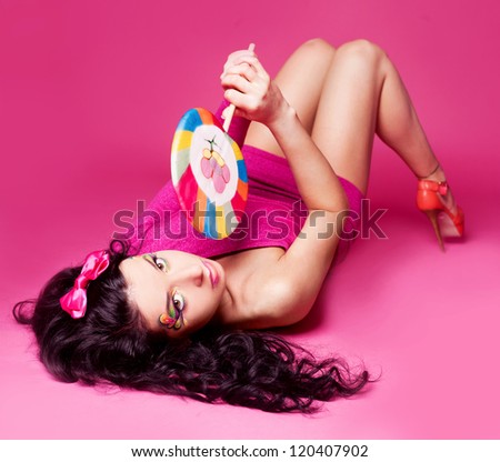 pretty young brunette woman with a lollipop, isolated against pink background