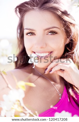 beautiful young brunette woman with a flower in her teeth standing near the apple tree on a warm summer day