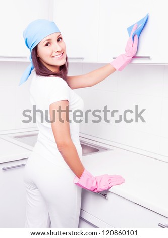 beautiful young housewife cleaning the furniture in the kitchen