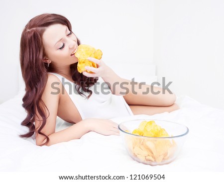happy young woman eating potato chips in bed at home