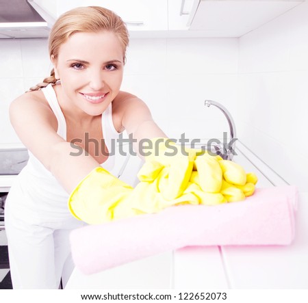 beautiful happy young housewife cleaning the furniture in the kitchen at home