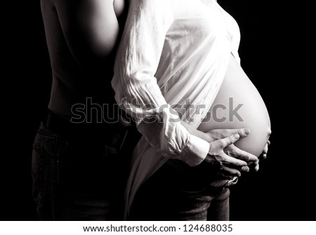 black and white picture of the hands and torso of a pregnant woman and her husband, isolated on black studio background