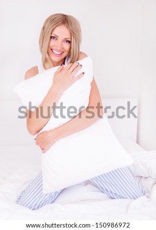 beautiful young woman wearing pajamas holding a pillow  in bed at home