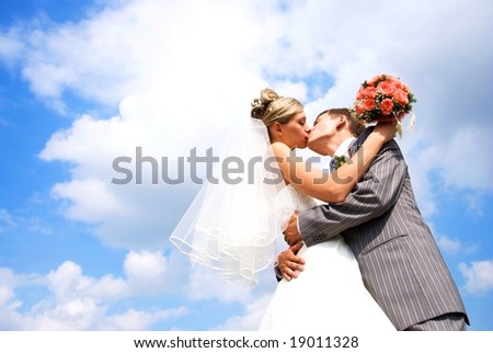 young bride and groom kissing against blue sky with clouds