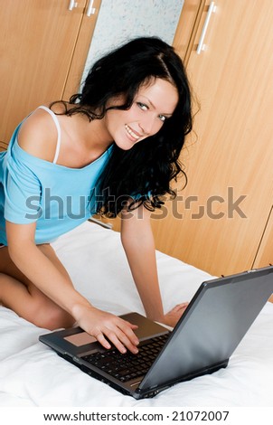 beautiful cheerful brunette girl with a laptop on the bed at home
