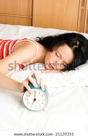 beautiful young brunette woman switches off the alarm clock in the morning and keeps sleeping