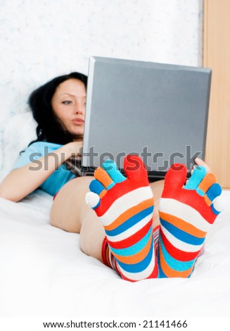 young brunette woman wearing funny socks with a laptop on the bed