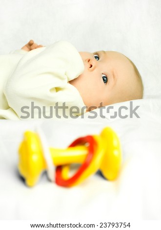 cute four months old baby boy on the bed with a colorful toy (focus on the baby)