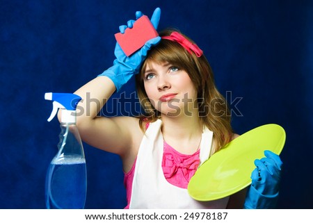 beautiful young tired housewife cleaning the dishes against blue background