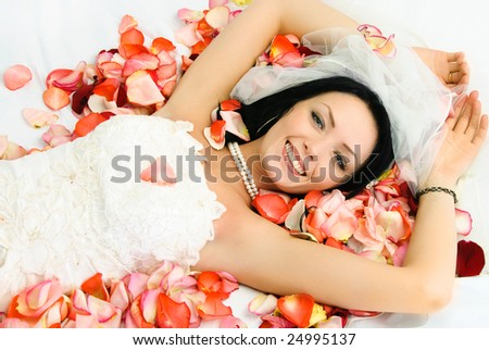happy beautiful brunette bride on the bed covered with rose leaves