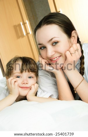 happy mother and her little daughter lie on the bed at home