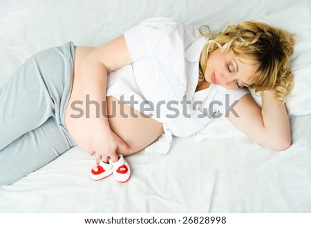 beautiful young pregnant woman in bed with tiny bootees for her future baby