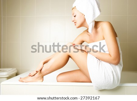 beautiful happy woman pampering herself and applying body lotion in the bathroom after the shower