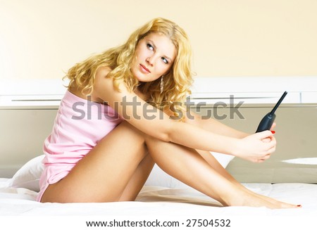 beautiful young worried woman sitting on the bed at home and holding a telephone in her hands