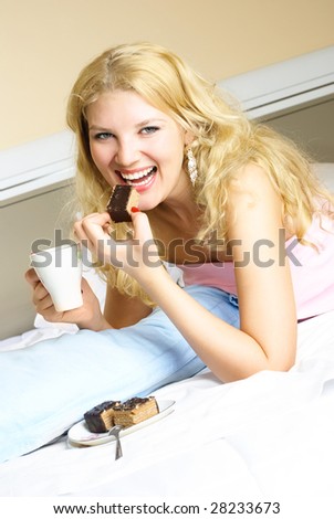 happy beautiful blond girl drinking tea with a cake in her bed at home
