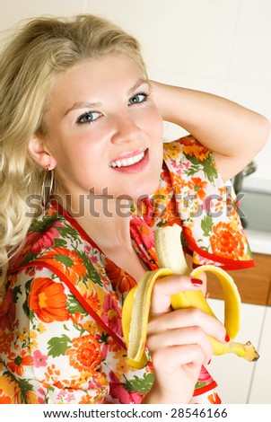happy beautiful young woman eating a banana at home in the kitchen