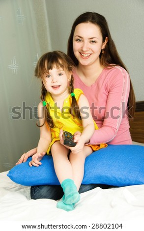 young beautiful mother and her little daughter watching TV