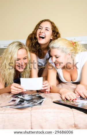 three happy friends lie on the bed and look through old photographs