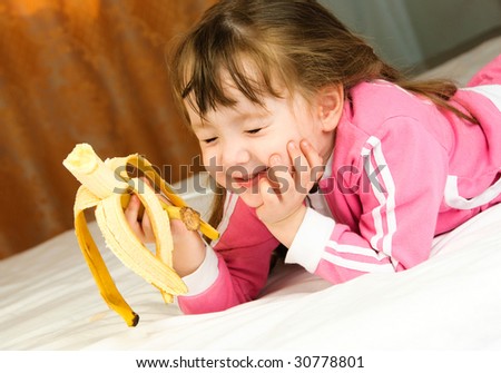 cute little girl eating a banana on the bed at home