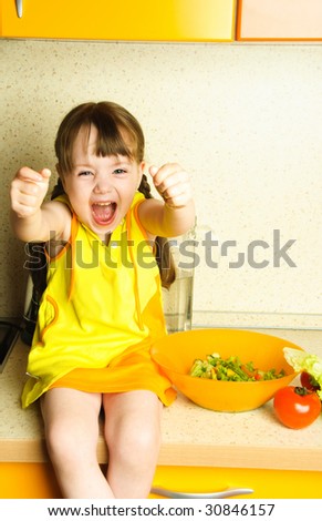 cute excited little girl making salad in the kitchen