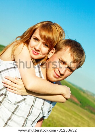 happy couple outdoor, young man giving his girlfriend piggyback ride