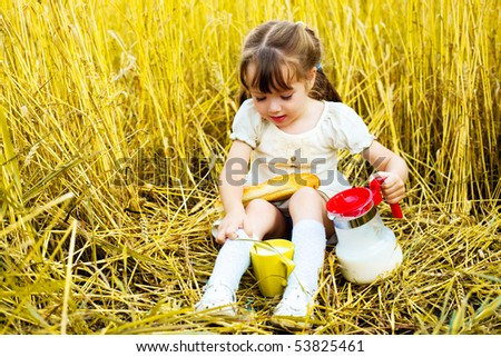 happy cute little girl in the wheat field eating a long loaf and drinking milk