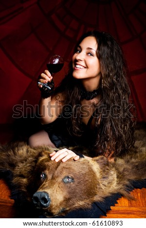 luxurious young brunette woman drinking vine on the bear skin rug