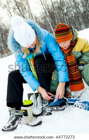 happy young mother and her son tightening laces and getting ready to go ice-skating