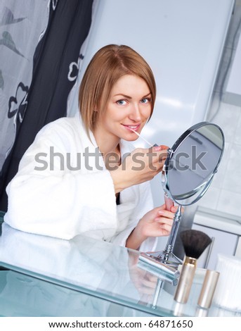 beautiful young woman looking into the mirror and applying lip gloss