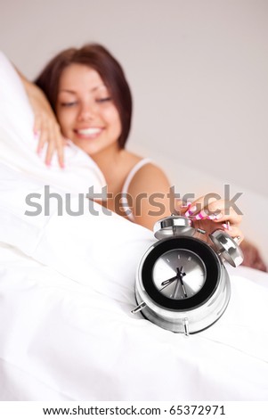 pretty happy girl waking up in the morning and switching off the alarm clock (focus on the clock)
