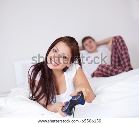 happy young girl playing computer games and her man looking bored (on the background)