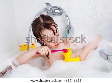 cute little girl taking a bath with foam and brushing teeth to her toy duck