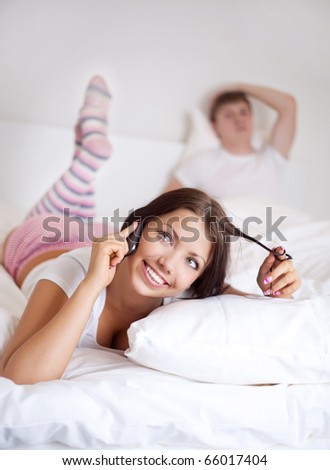 happy young woman talking on the phone and  sleeping man on the bed at home (focus on the woman)