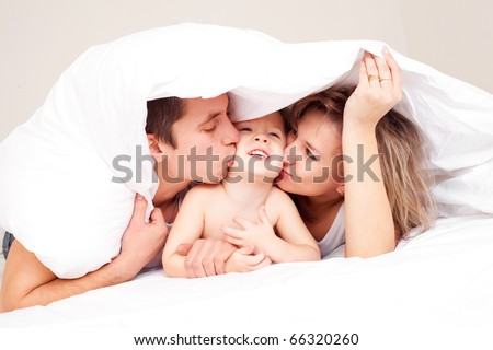 happy family, mother ,father and their baby under the blanket on the bed at home