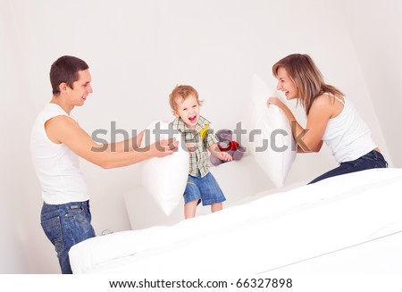 happy family, mother ,father and their baby having a pillow fight on the bed at home (focus on the baby)
