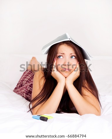 unhappy girl with a note book on her head tired of doing homework on the bed at home