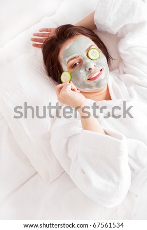 young woman wearing a deep cleansing green clay mask on her face and cucumbers on her eyes