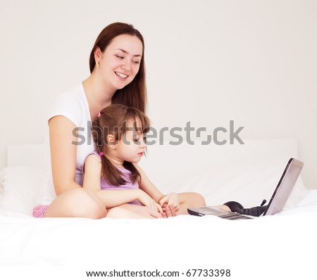 beautiful young mother and her five year old daughter with a laptop on the bed at home