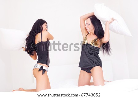 to happy laughing  girls having a pillow fight on the bed at home