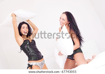 to happy laughing  girls having a pillow fight on the bed at home