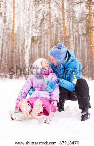 happy family; young mother and her daughter with a sled having fun in the winter park