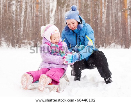 happy family; young mother and her daughter with a sled having fun in the winter park (focus on the child)