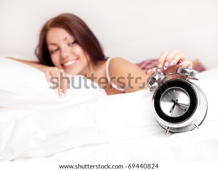 pretty brunette girl waking up and switching off the alarm clock (focus on the clock)