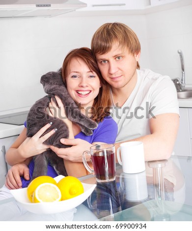 happy young couple with a cat drinking tea with lemon in the kitchen at home