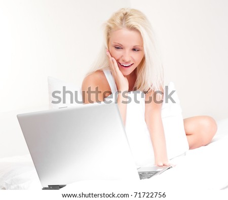 happy blond girl with a laptop on the bed at home